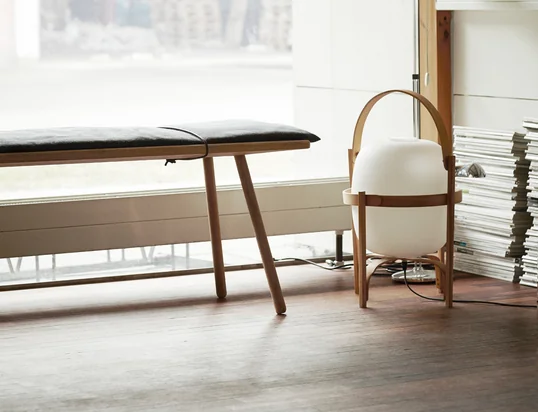 Le banc Georg de Skagerak dans la vue d'ambiance : Le banc élégant est extrêmement pratique dans la vie quotidienne et peut être parfaitement combiné avec une lampe placée sur le sol.
