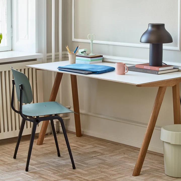 The Revolt Chair, noir / vert pétrole par HAY sur un bureau