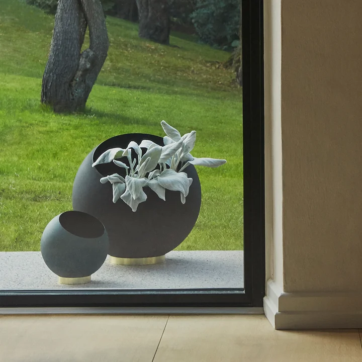 Le pot de fleurs Globe de AYTM dans ses différentes tailles derrière une fenêtre du sol au plafond à l'extérieur