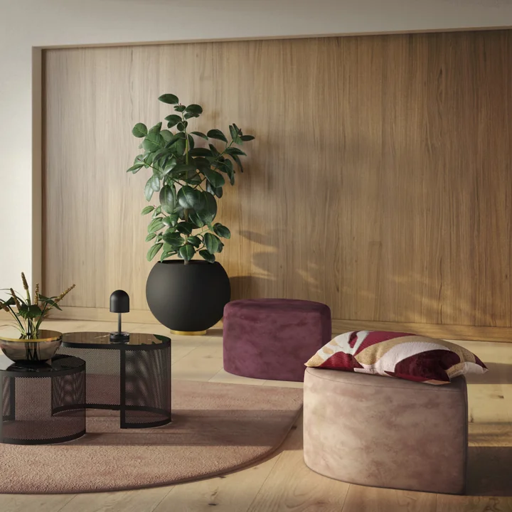 Le pot de fleurs Globe de AYTM avec une plante d'intérieur haute à côté des poufs Stilla de AYTM