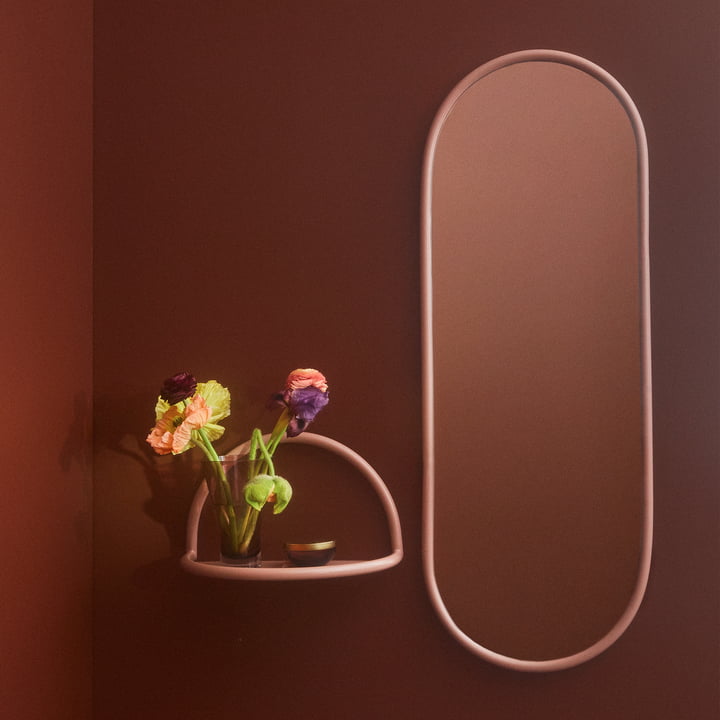 Le miroir mural Angui avec cadre rose de AYTM à côté d'une petite étagère murale de la même couleur.