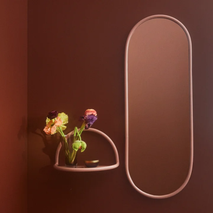 Le miroir mural Angui avec cadre rose de AYTM à côté d'une petite étagère murale de la même couleur.
