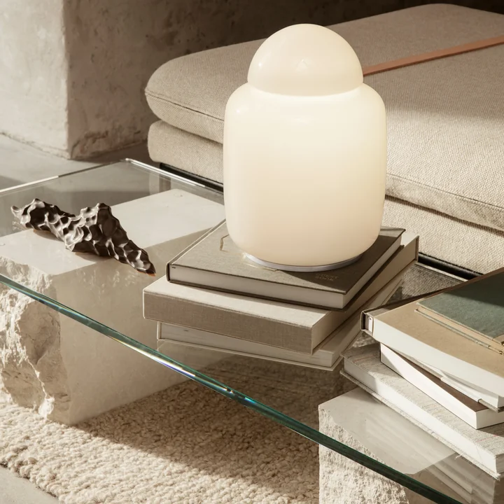 La lampe de table Bell de ferm Vivre sur des piles de livres sur une table basse en verre