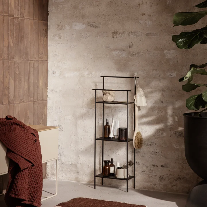 L'étagère de salle de bains Dora par ferm Vivre avec des accessoires de salle de bains à côté d'une grande plante d'intérieur