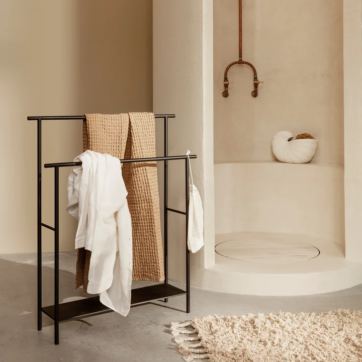 Le porte-serviettes Dora de ferm Vivre avec des serviettes à côté de la douche en pierre