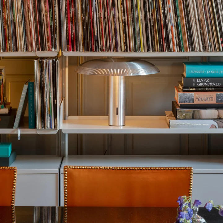 La lampe de table w203 Ilumina LED de Wästberg en aluminium sur une étagère blanche entre des livres et des cahiers.