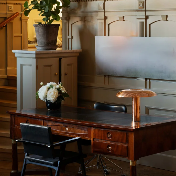 La lampe de table w203 Ilumina LED de Wästberg en cuivre sur un bureau antique dans une ambiance raffinée avec beaucoup de bois