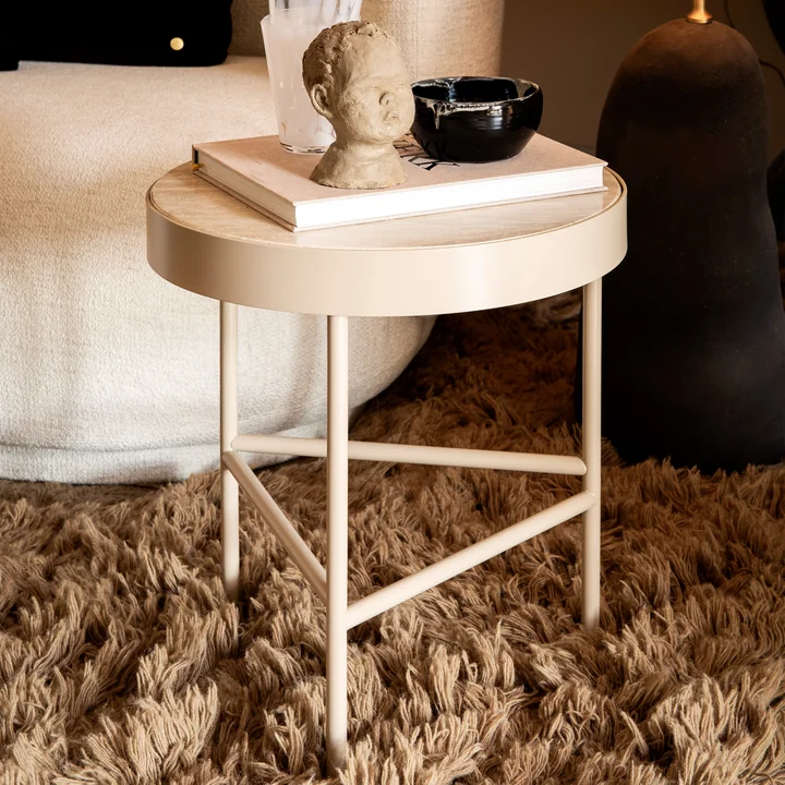 La petite table basse Travertine par ferm Vivre à côté d'un canapé avec des livres et des objets d'art