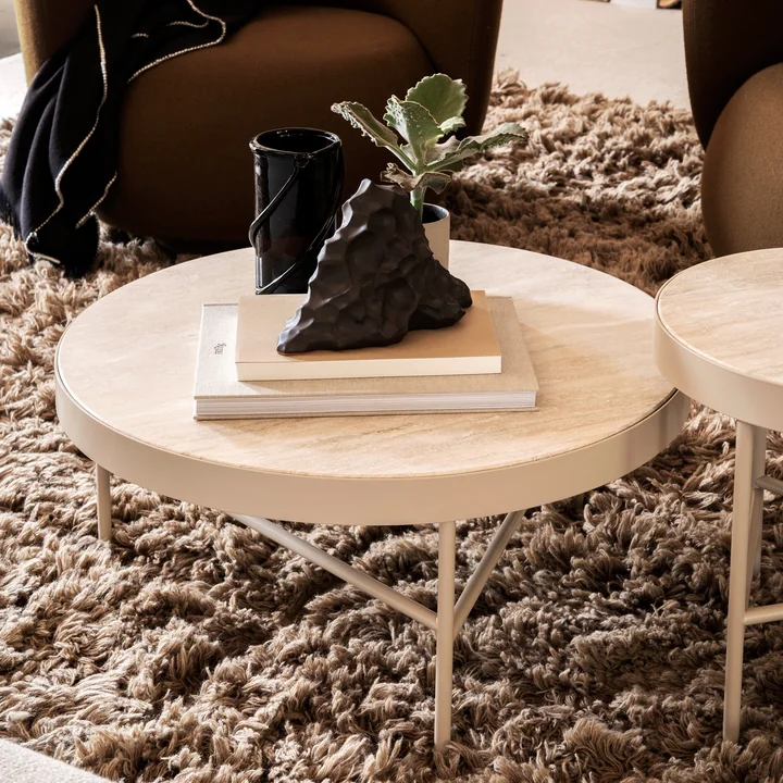 La grande table basse Travertine de Ferm Living with books and art objects on a fluffy carpet