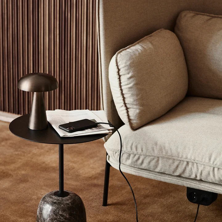 La lampe à accu Como SC53 de & Tradition sur une table d'appoint noire à côté d'un canapé clair