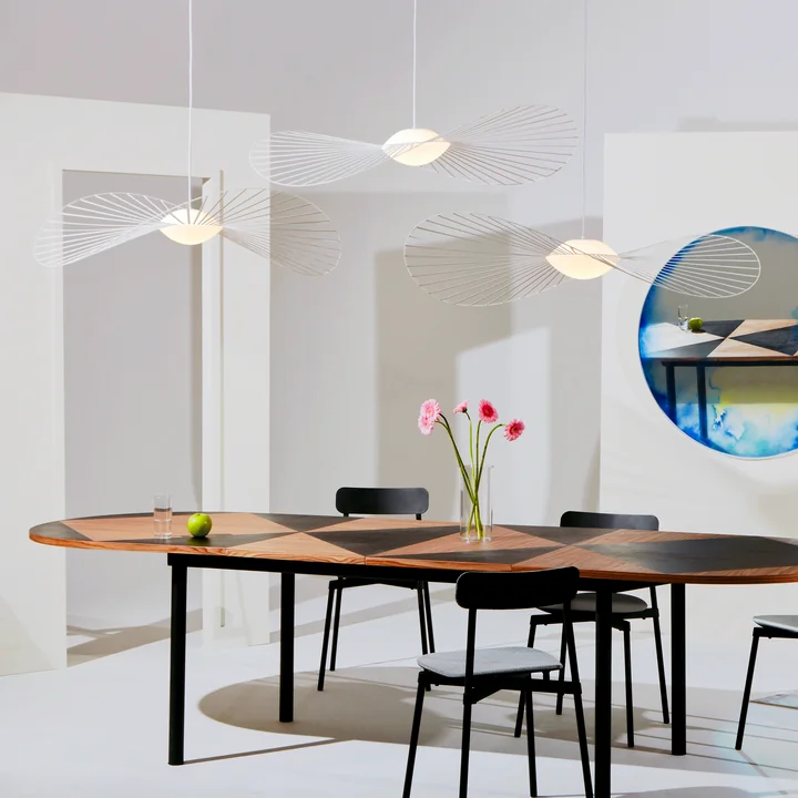 Le luminaire suspendu Vertigo Nova de Petite Friture en groupe au-dessus d'une table de salle à manger ovale en bois avec des chaises noires