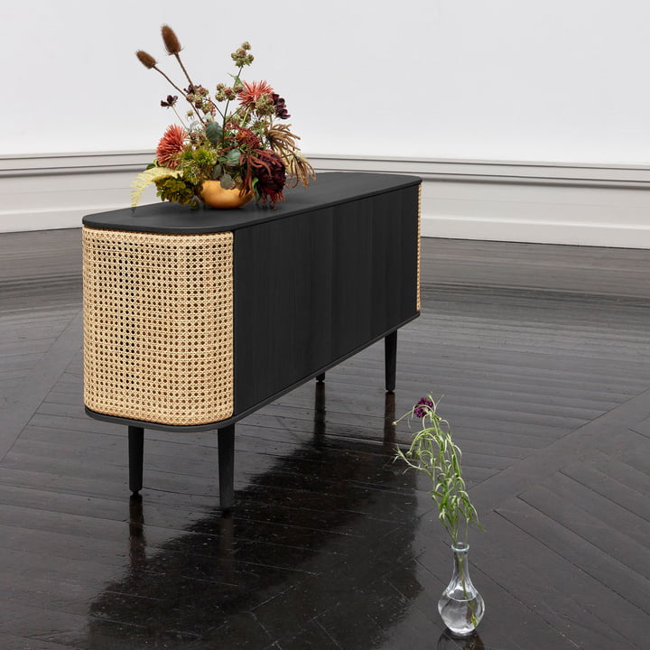 Le site Treasures Sideboard de Umage en noir / tressage viennois avec des fleurs sur un parquet noir