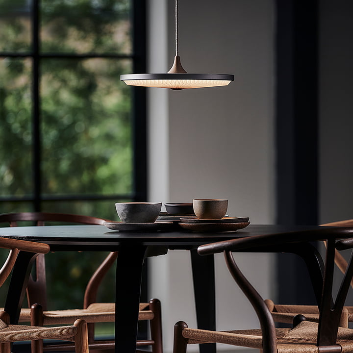 La lampe pendante à LED Soleil de Le Klint au-dessus d'une table à manger ronde sombre avec des chaises en bois