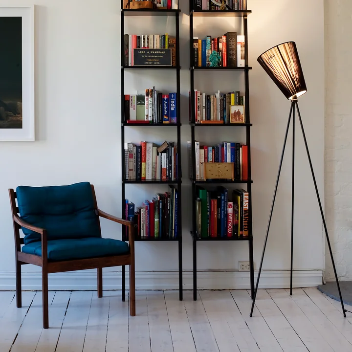 Le lampadaire Oslo Wood de Northern à côté des étagères et d'un fauteuil bleu pétrole
