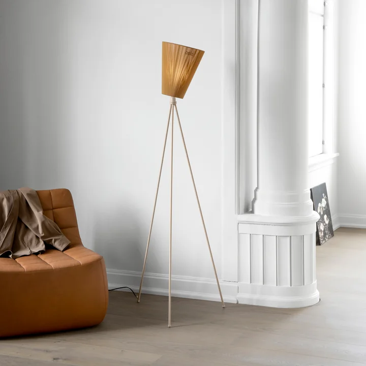 Le lampadaire Oslo Wood de Northern à côté d'un fauteuil en cuir brun et d'un mur blanc