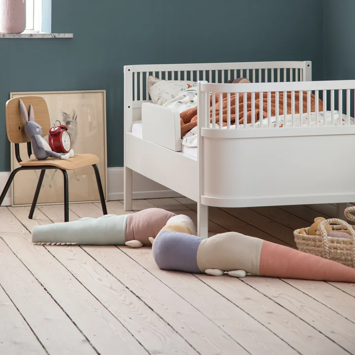 Le coussin ludique Sleepy Croc de Sebra à côté du lit d'enfant blanc