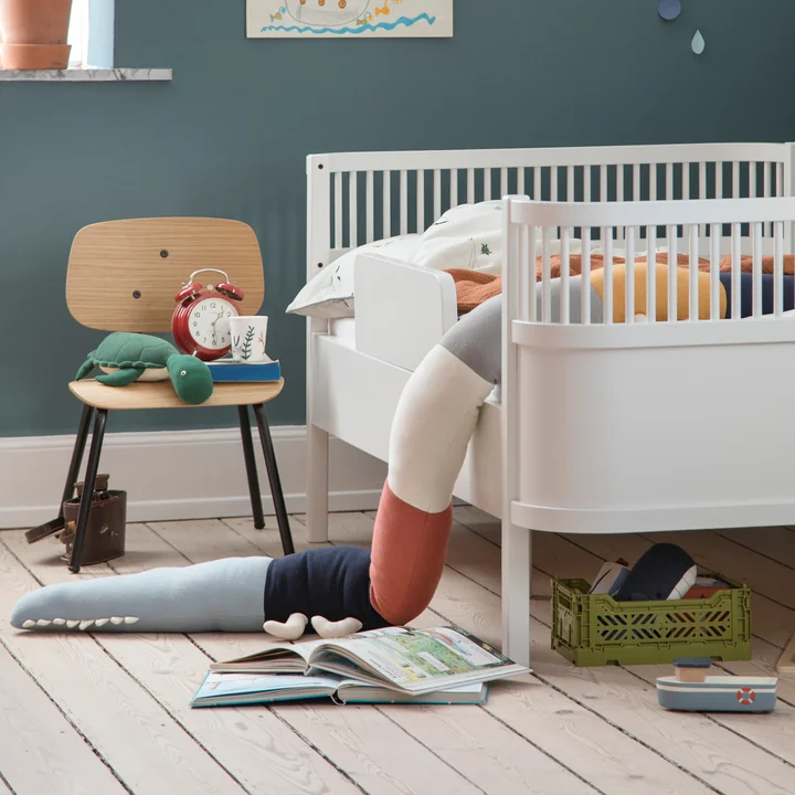 Le coussin Sleepy Croc et la chaise Oakee de Sebra à côté du lit d'enfant blanc